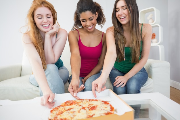 Happy young female friends eating pizza at home