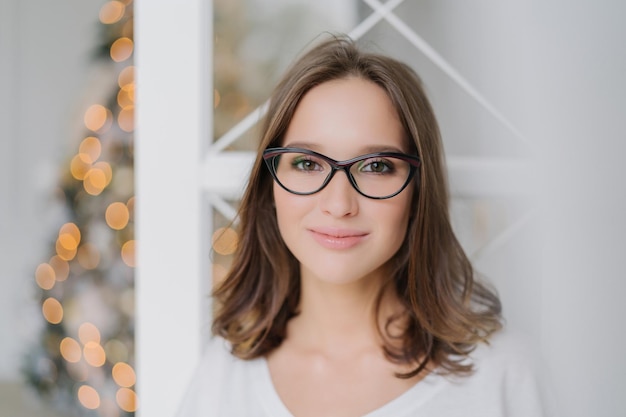 Photo happy young female model in spectacles charming smile poses by decorated christmas tree