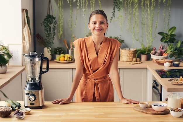 Happy young female in orange dress standing by kitchen table