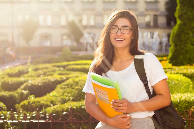 Happy young female student with books in the hands on the university background. 