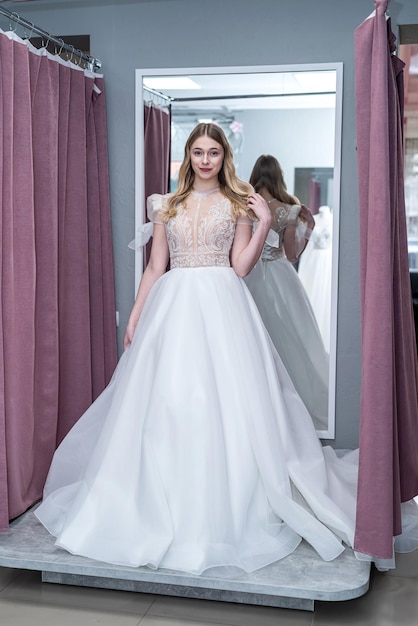 Happy young female tailor is trying on an elegant wedding dress in bridal Boutique