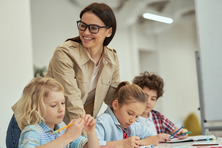 Photo happy young female teacher in glasses helping her little students in a classroom kids sitting at