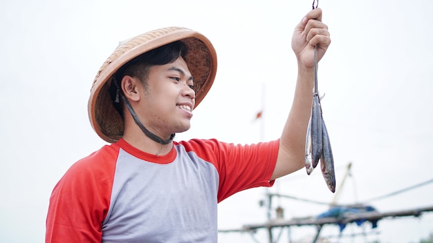 Happy young fisherman on the beach holding his catch fish and shows in front of his boat