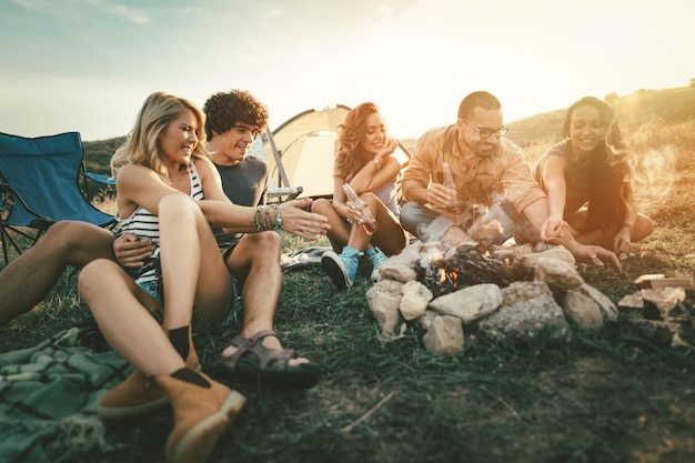 Счастливые молодые друзья наслаждаются солнечным днем на горе. Они смеются и разводят костер возле палатки.
