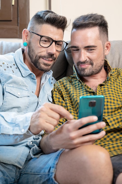 Foto felice giovane coppia gay utilizzando il telefono cellulare mentre era seduto su un divano nel soggiorno