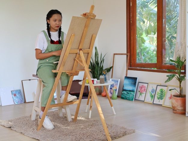 Foto felice giovane ragazza che disegna con una tavolozza di colori e un pennello a casa artista di pittura