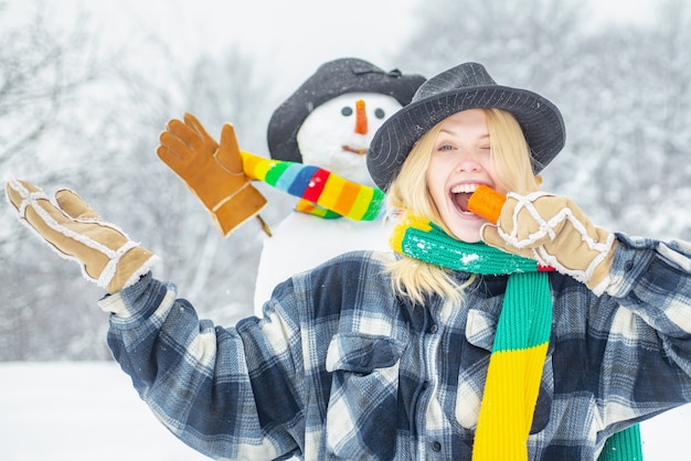 happy young girl eating a carrot near a snowman outdoors