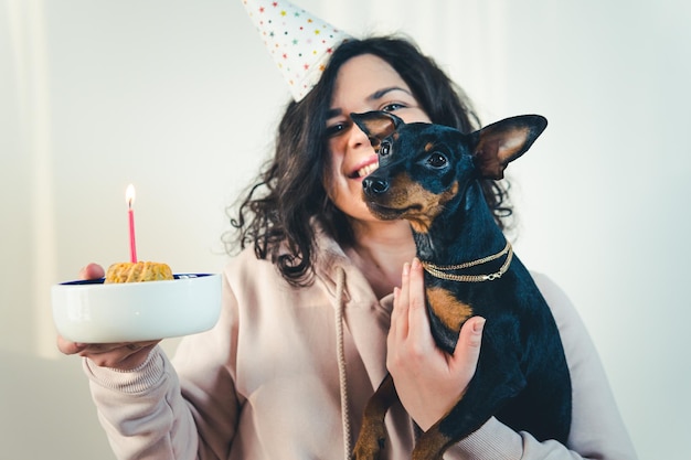 Счастливая молодая девушка дает домашний торт своей собаке в помещении