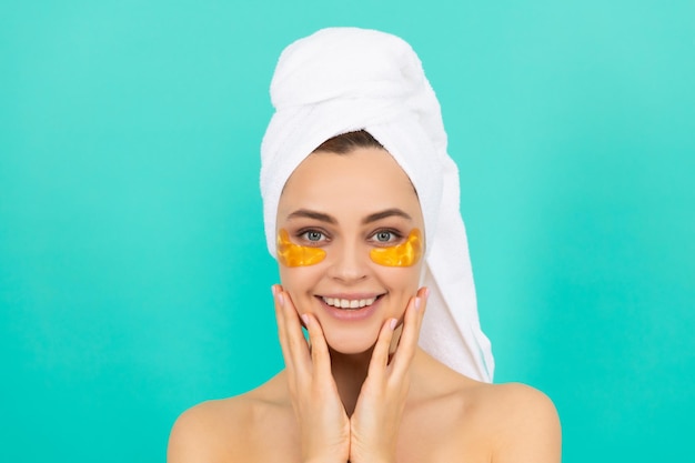 Happy young girl has collagen gold eye patches on face with towel