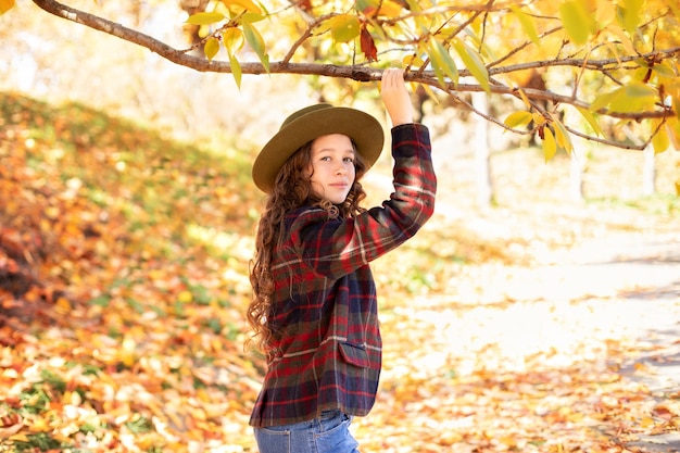 Happy young girl in hat and autumn clothes on an autumn background with falling golden leaves