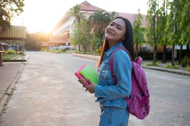 Счастливая молодая девушка держит книгу с рюкзаком, гуляя по школе