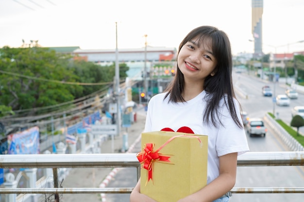 Happy young girl hold gift box on city view background.