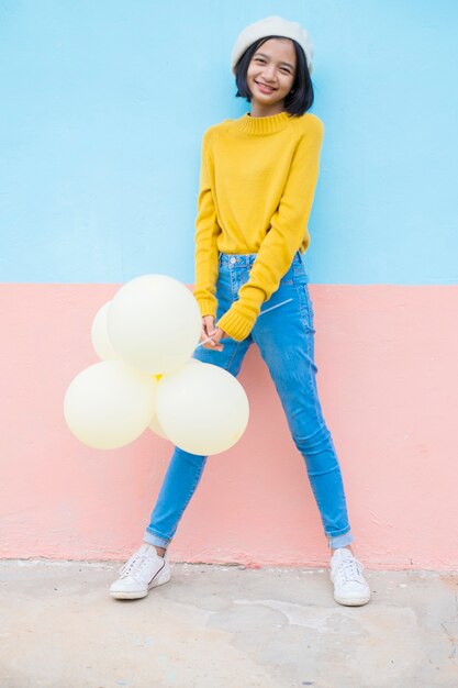 Happy young girl hold yellow balloon wear yellow sweater smile over blue background.