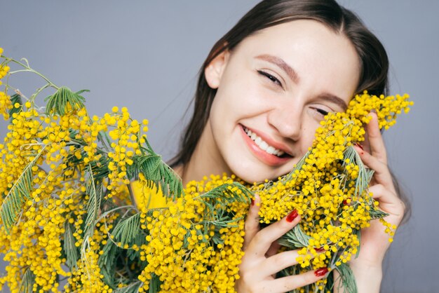 Happy young girl holding a big bouquet of yellow mimosa and laughing