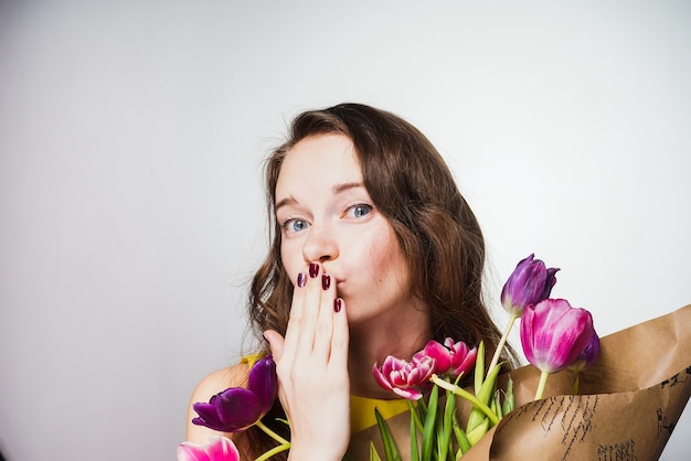 花の花束を手に持って、エアキスを送って、世界の女性の日を祝う幸せな少女