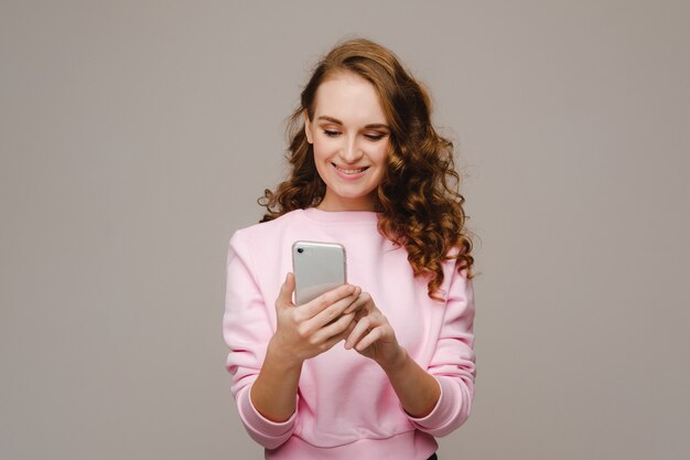 電話を持っている幸せな若い女の子がそれを見て微笑む。