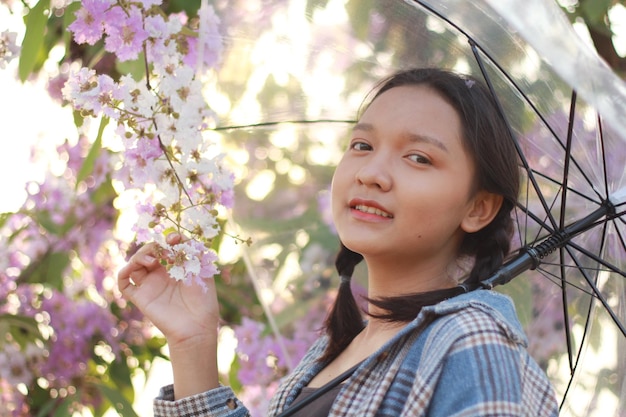 Ragazza felice che tiene un ombrello in piedi sotto un bellissimo albero con fiori.