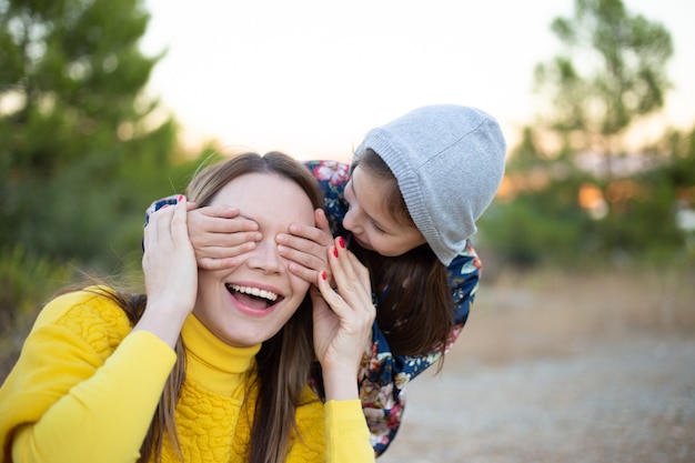 彼女の手で彼女の母親の目を覆って笑って幸せな若い女の子