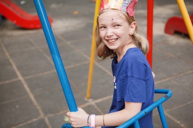 Happy young girl laughing joyfully, sitting on a swing on playground