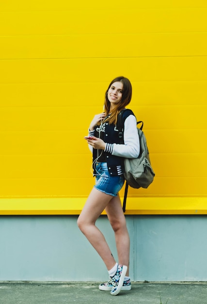 Happy young girl listening music in headphones over yellowwall