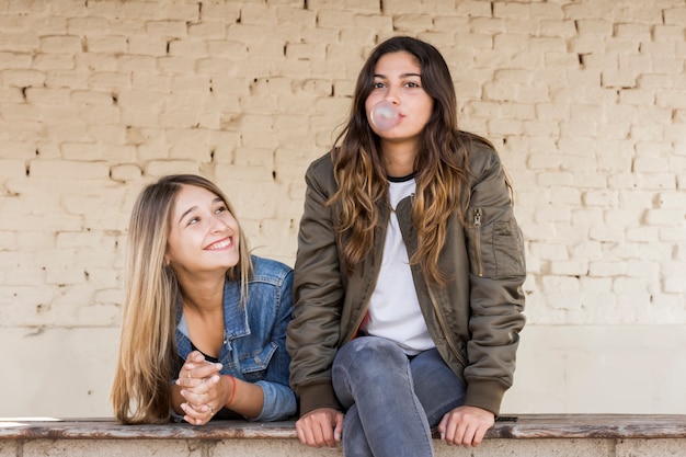 Happy young girl looking at her friend blowing bubble gum