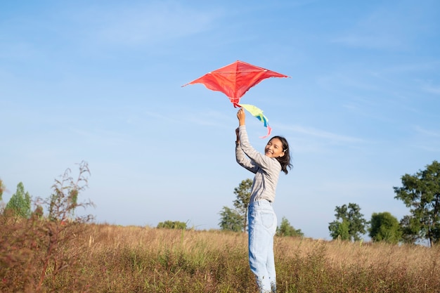 幸せな若い女の子は青い空と牧草地で凧を再生します