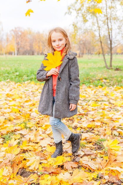 Happy young girl playing with falling yellow leaves