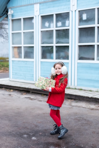 Happy young girl in red coat standing at street with christmas presents at winter day