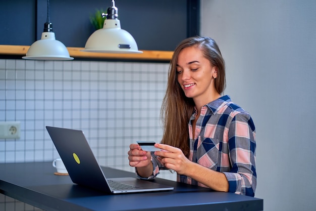 Happy young girl shopper shopaholic shopping online and paying for goods and purchases using credit card and laptop. E-commerce