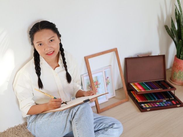 Happy young girl siting at home and drawing with a paint palette and a paintbrush painting artist