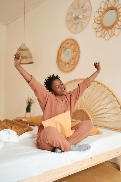 Happy young girl sitting on bed in bedroom and using laptop muslin pajama chatting with friends