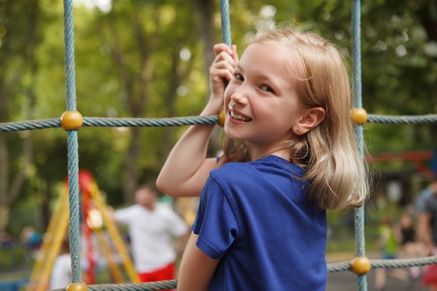 Happy young girl smiling over her shoulder while climbing net on playground