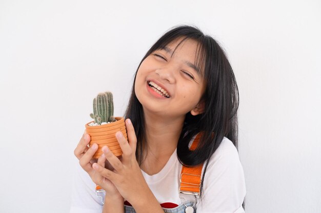 Счастливая молодая девушка улыбается и показывает кактус на белом фоне