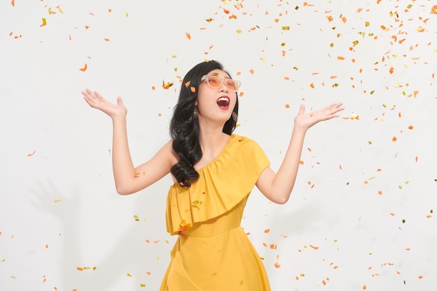 A happy young girl in summer clothes standing under confetti rain isolated over white background