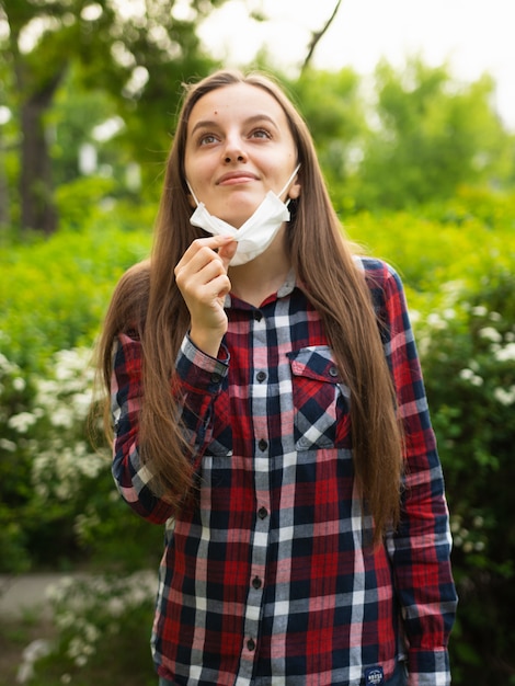 写真 幸せな若い女の子は医療用マスクを脱いで自然の中で新鮮な空気を呼吸します