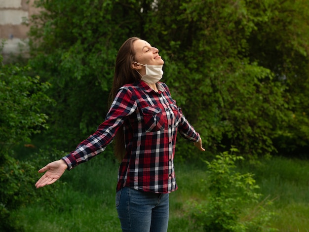 Happy young girl takes off a medical mask and breathes fresh air in nature