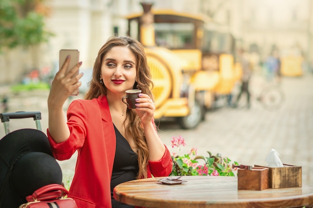 Счастливая молодая девушка принимая selfie в кафе на открытом воздухе.