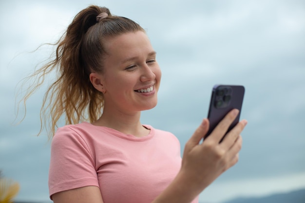 幸せな若い女の子は、家のバルコニーの街の背景の女性の屋根の上で自分撮りをする携帯電話を使用します。