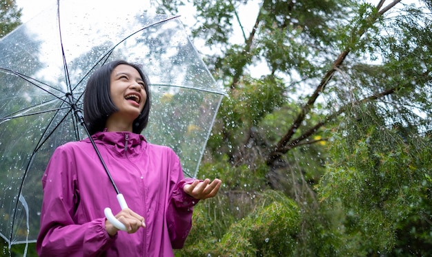 幸せな若い女の子は雨の中で傘とレインコートを着ています。