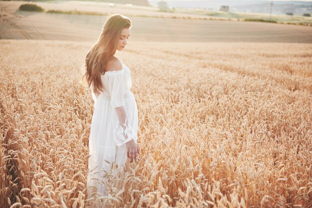 Happy young girl with long, beautiful hair standing in a wheat field under the sunlight