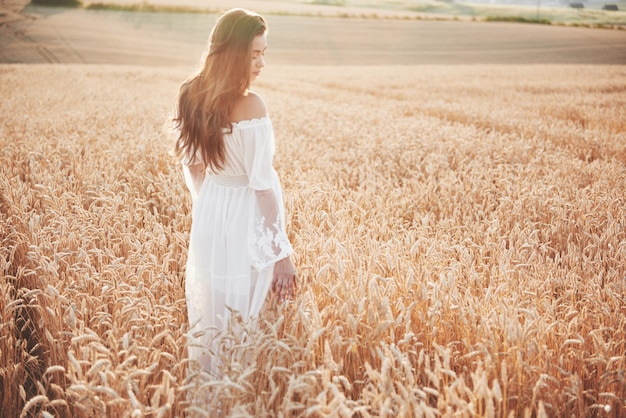 Happy young girl with long, beautiful hair standing in a wheat field under the sunlight