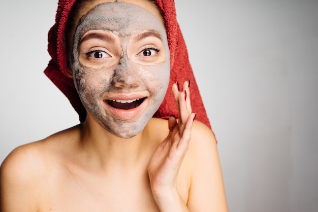 Happy young girl with a towel on her head applied a useful clay mask on her face