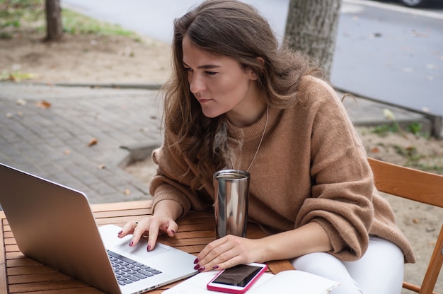 Фото Счастливая молодая девушка, работающая в кафе с ноутбуком