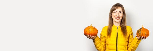 Happy young girl in a yellow jacket holds two pumpkins