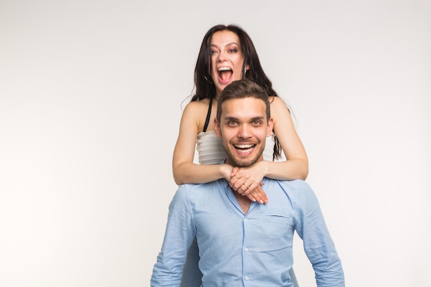 Happy young girlfriend jumps on the back of her boyfriend on white background