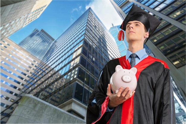 Happy young graduation man with piggy bank