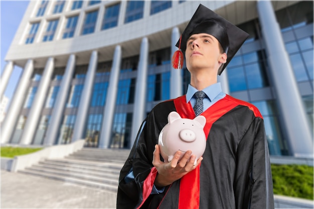 Happy young graduation man with piggy bank