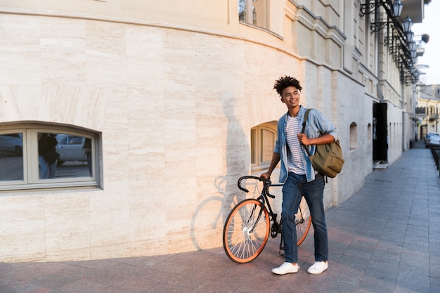 Happy young guy walking with bicycle outdoors on the street