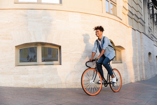 Happy young guy walking with bicycle outdoors on the street