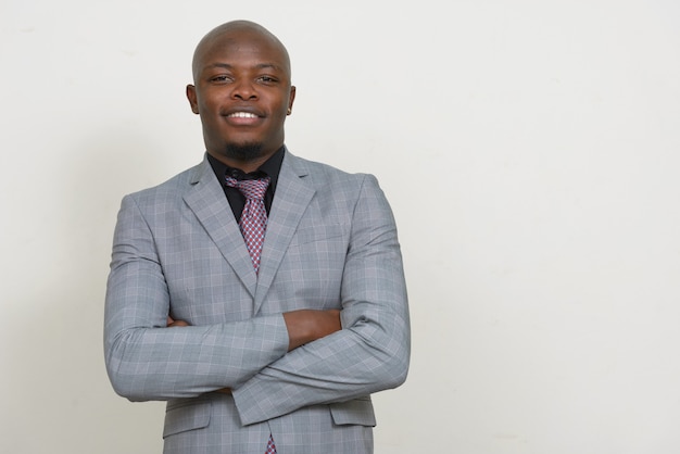 Happy young handsome bald African businessman smiling with arms crossed